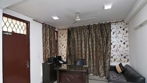 A room with a desk, a sofa, a ceiling fan, and patterned curtains. - Gurugram Home Residency (Gurugram)