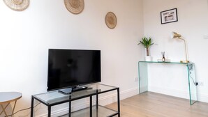 A modern living room with a flat-screen TV on a glass table, a glass console table with decorative items, and woven wall art. - Brixton/2bed Flat/privateterrace/tv/wifi (London)