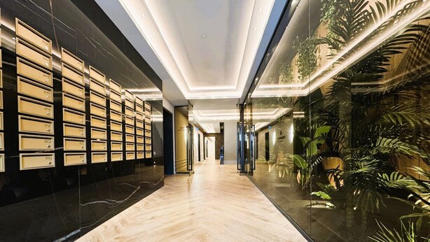 Un moderno vestíbulo de hotel con piso de mármol, un muro de cristal con plantas y una fila de casilleros numerados a la izquierda.