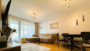Una sala de estar moderna con un sofá modular, una mesa de comedor con sillas, un piano y una araña.