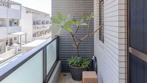 A balcony with a potted plant, two wooden stools, and a view of neighboring buildings. - Turn Right Home (Wujie)