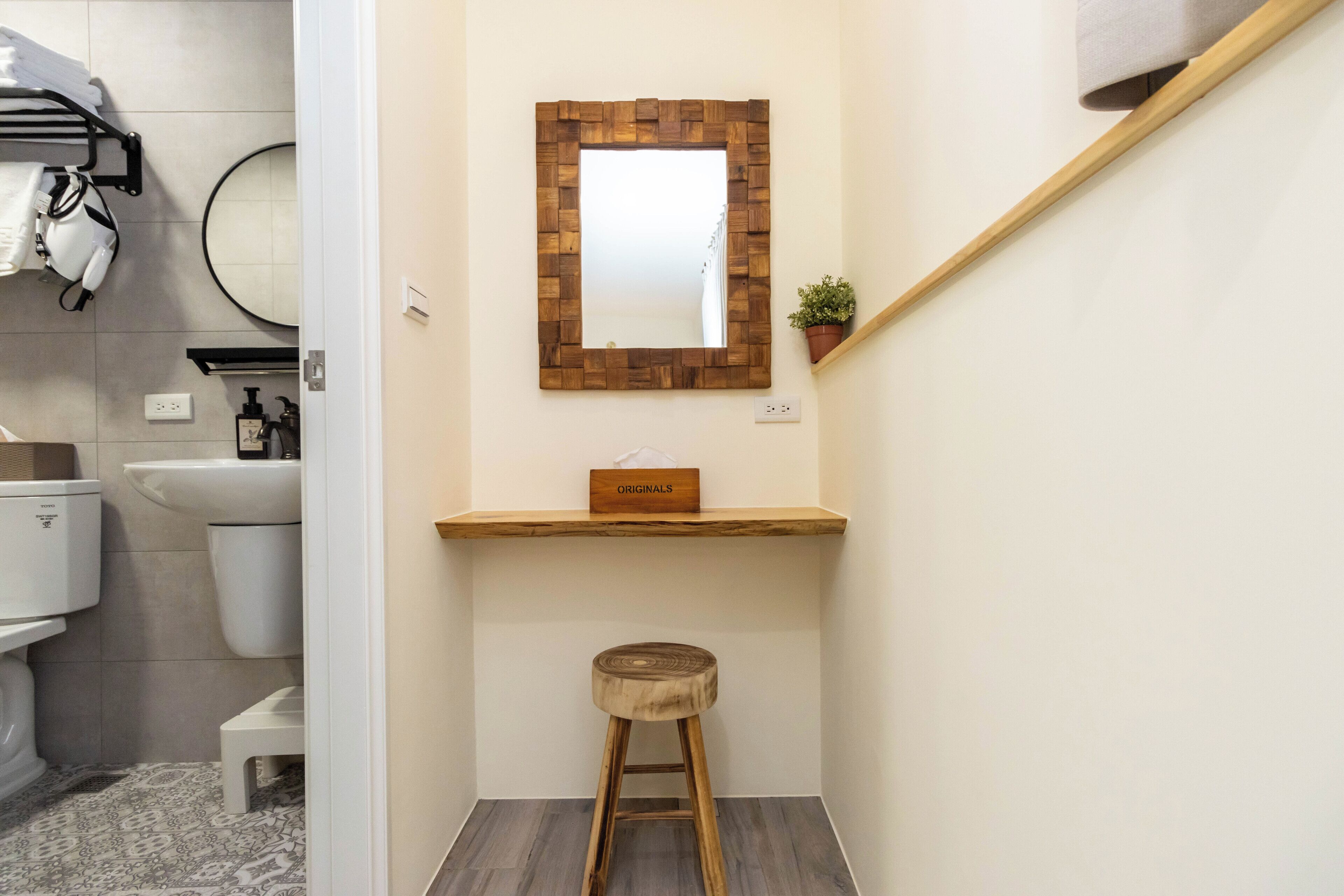 Un baño con un espejo de marco de madera, un taburete pequeño, una estantería con un cartel, un inodoro y un lavabo.