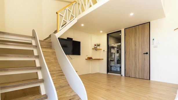 A modern interior with a wooden staircase, a flat-screen TV mounted on the wall, and a sliding door leading to a bathroom. - Turn Right Home (Wujie)