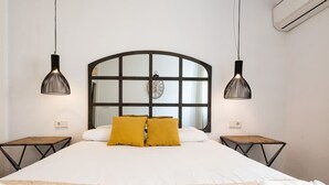 A bedroom with a large bed, two bedside tables, a window with a clock, and two pendant lights.