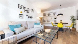A modern living room with a sofa, a glass coffee table, and a dining area with yellow chairs.