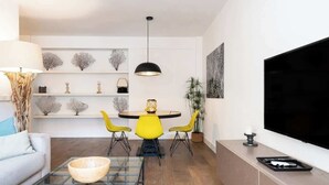 A modern living room with a sofa, coffee table, yellow chairs, a dining table, and a TV.