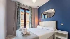 A neatly made bed with white linens and a gray throw blanket, a bedside table with a lamp, and a large mirror on the wall. - Unique Charming Apartment in the Heart of Málaga (Málaga)