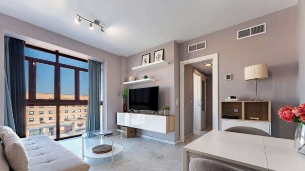 A modern living room with a sofa, a coffee table, a TV on a white cabinet, and a dining table with chairs. - Unique Charming Apartment in the Heart of Málaga (Málaga)