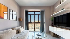 A modern living room with a sofa, a glass coffee table, a flat-screen TV, and a large window with curtains. - Unique Charming Apartment in the Heart of Málaga (Málaga)