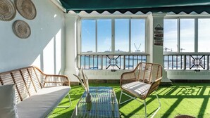 A sunlit room with a view of the sea, featuring wicker furniture, a glass coffee table, and a sign with directional arrows.