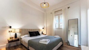 A modern hotel room with a large bed, bedside tables, a mirror, and a window with curtains.