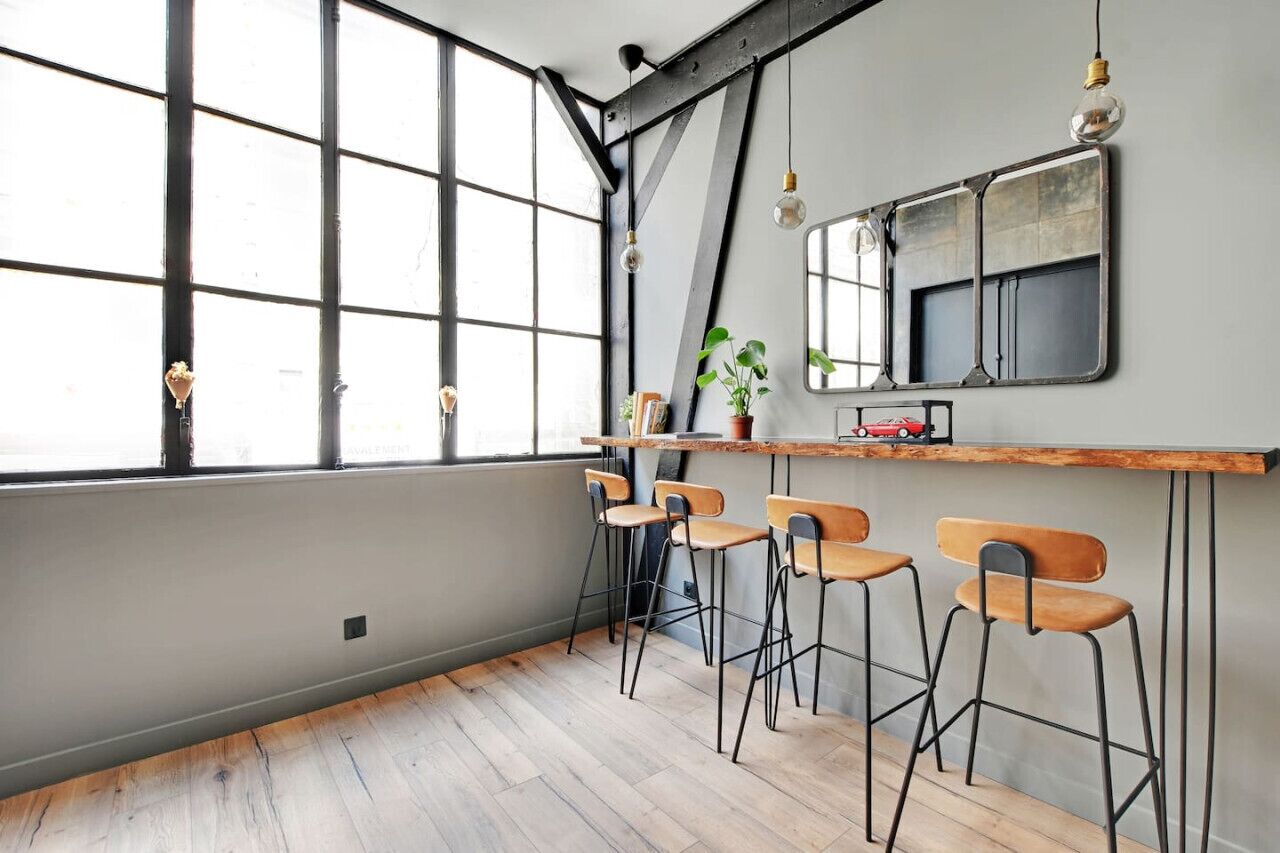 A modern kitchen with a large window, bar stools, and a wooden countertop.