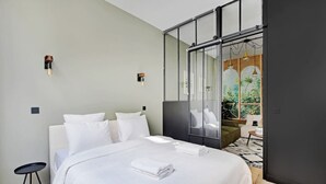 Une chambre d’hôtel moderne dotée d’un grand lit, d’une petite table de chevet, d’un canapé et d’une porte vitrée donnant sur un balcon avec vue sur la verdure.