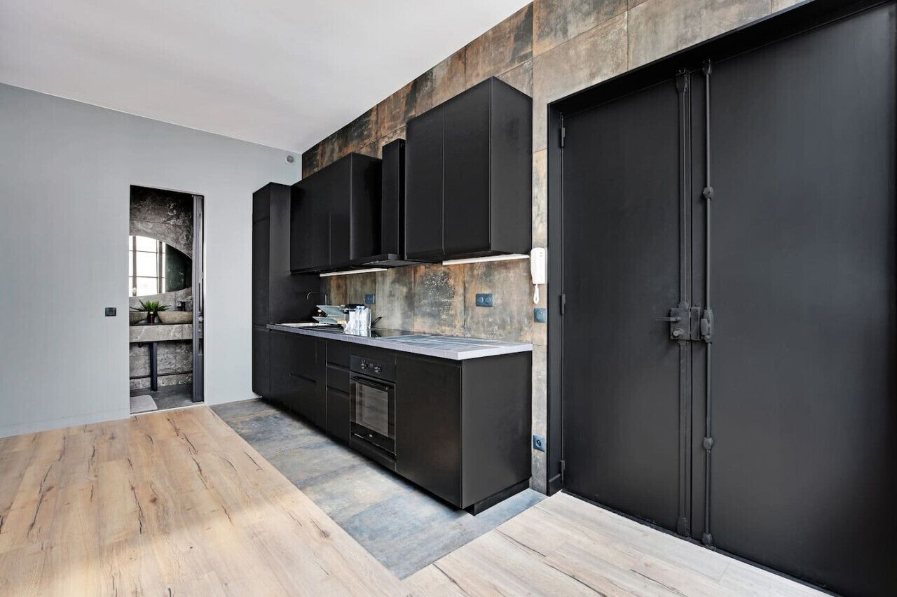 Una cuina moderna amb armaris foscos, una illa central i una porta gran de color negre.