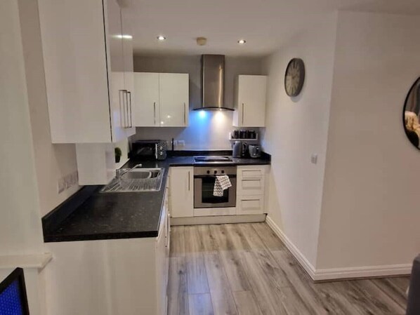 A modern kitchen with white cabinets, a stainless steel range hood, and a built-in oven.