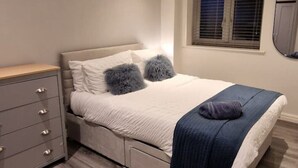 Een slaapkamer met een bed, een dressoir, een raam en een spiegel.