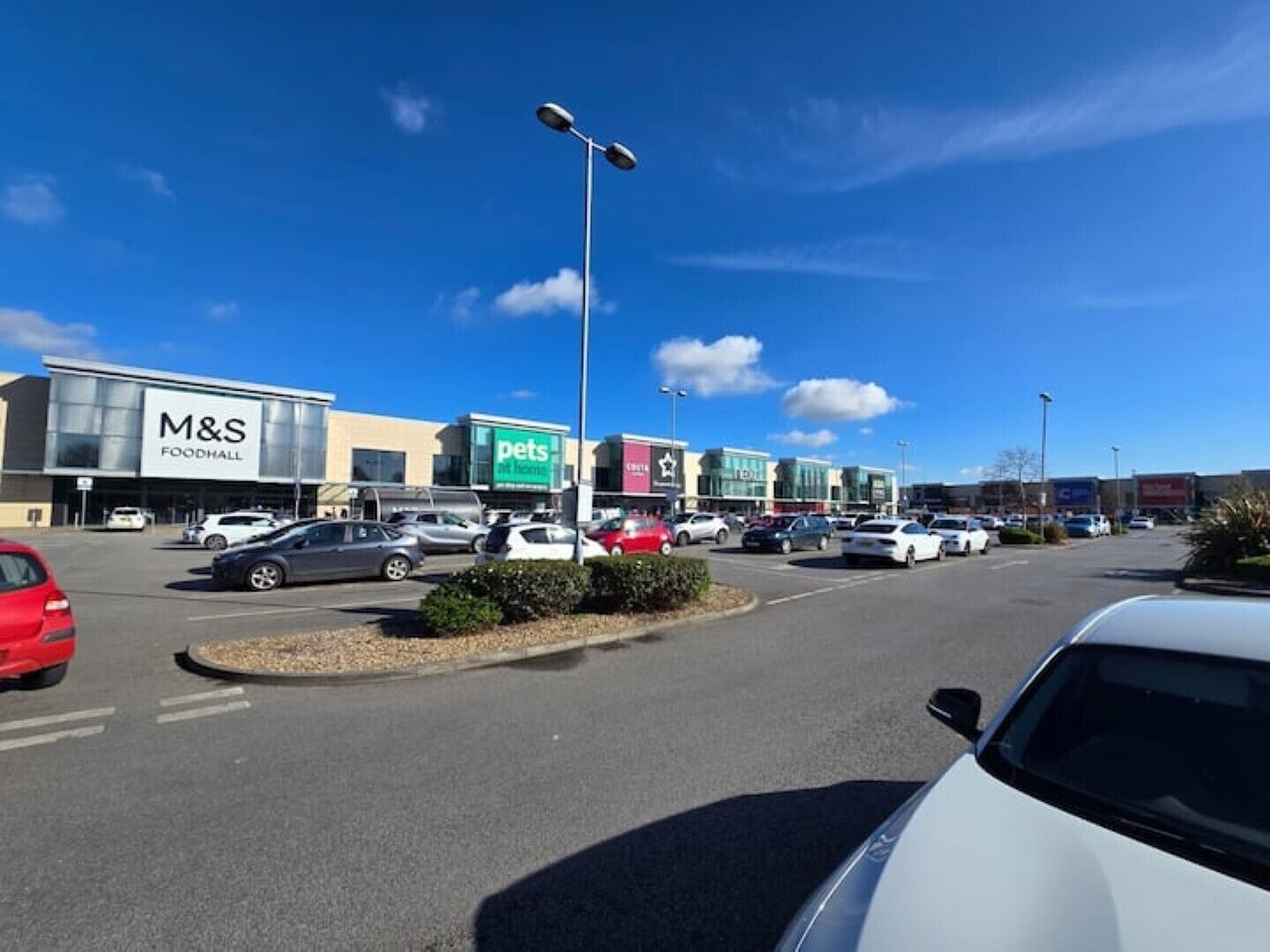 A parking lot with several cars, a M&S Food Hall, and a Pets at Home store.