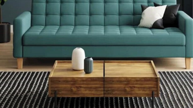 Een smaragdgroene bank met een houten salontafel ervoor, tegen een donkere muur.