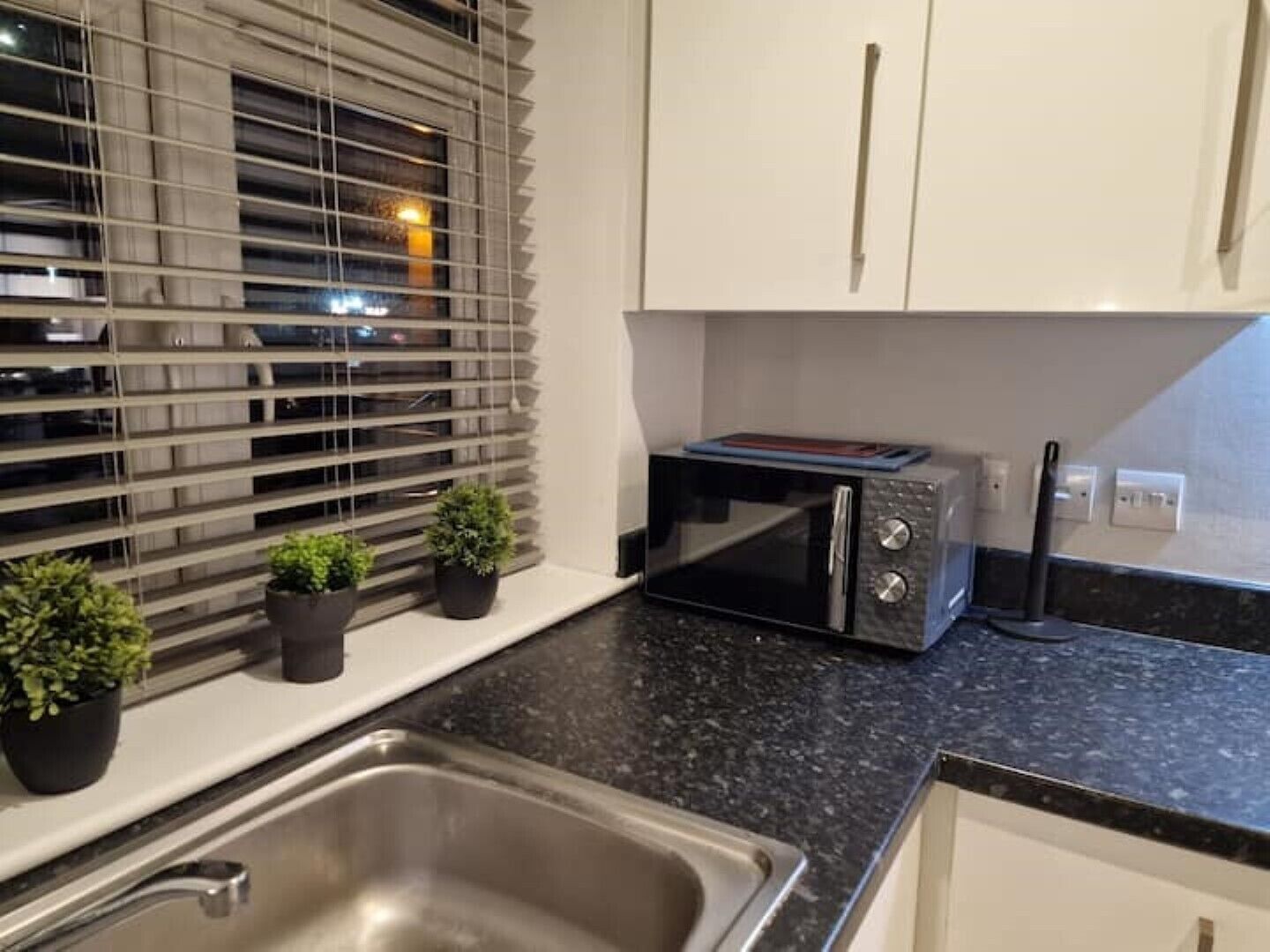 A modern kitchen with a stainless steel sink, a built-in microwave, and potted plants on the windowsill.