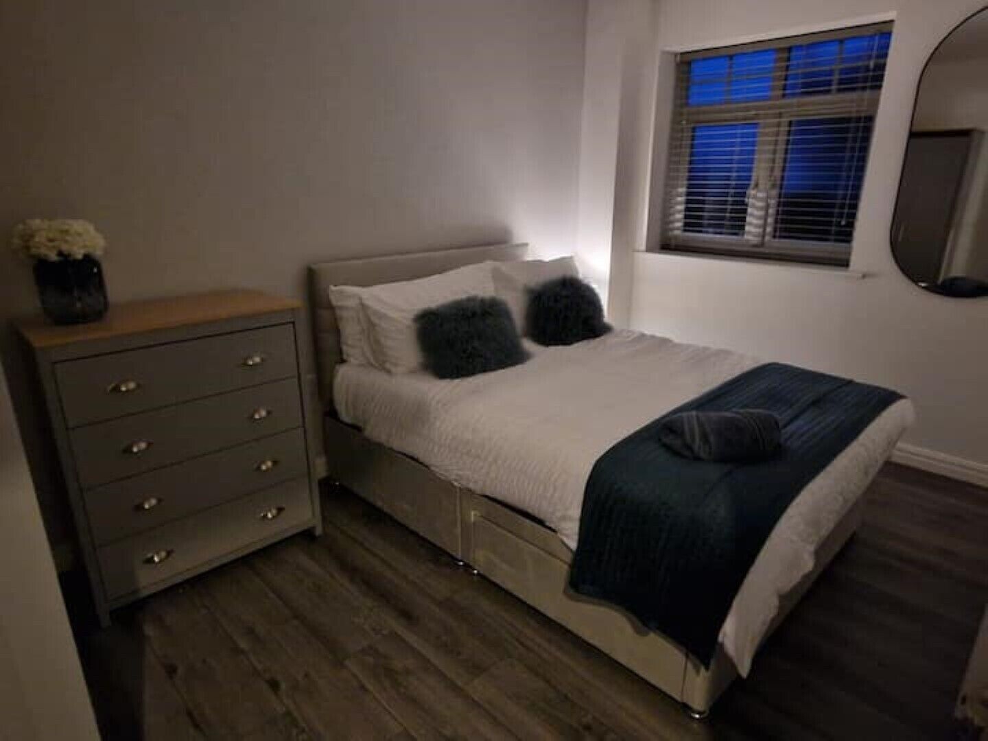Un dormitorio con cama, cómoda, ventana con persianas y espejo en la pared.
