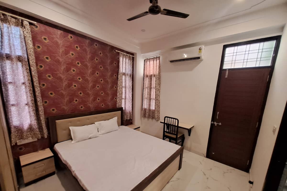 A bedroom with a bed, a chair, a wardrobe, a ceiling fan, and a window with curtains.