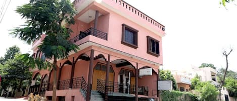 Ein zweistöckiges, pinkfarbenes Gebäude mit Balkon und Treppe, vor der ein Motorrad geparkt ist.
