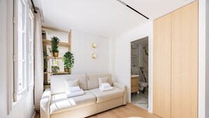 A modern living room with a beige sofa, a round coffee table, and a wooden wardrobe. There is a bathroom visible through an open door. - Bail Mobilité - New Renovated Studio Invalides EiffelTower Paris 7 (Paris)