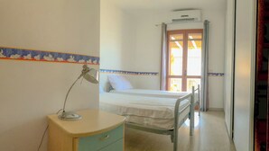 Una habitación pequeña y sencilla con una cama, un escritorio con lámpara y una ventana con cortinas.