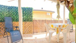 Un patio al aire libre con una mesa y sillas, rodeado por una valla de bambú y un seto verde.