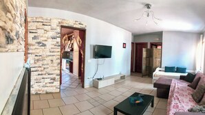 Una sala de estar con televisor, sofá, una mesa de centro y una cocina visible a través de un arco.