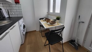 Une cuisine compacte équipée d’un lave-linge, d’une table à manger avec des chaises et d’une fenêtre.