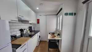 Une cuisine compacte avec des meubles blancs, un plan de travail en bois, un lave-linge encastré et un coin repas comprenant une table et des chaises.