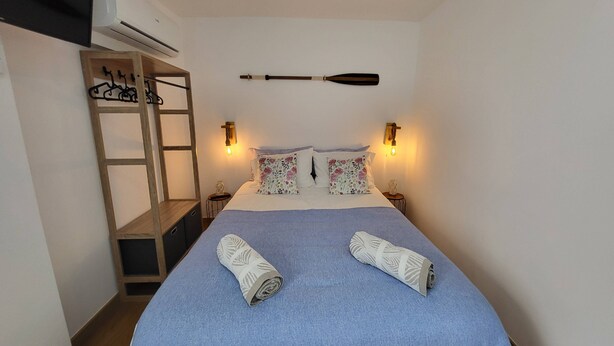 Une chambre à coucher avec un lit, une étagère en bois, deux lampes fixées au mur et un ventilateur de plafond.