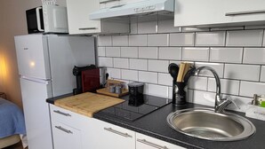 Une cuisine compacte avec des meubles blancs, un plan de travail noir, un évier en acier inoxydable et un micro-ondes posé sur un réfrigérateur blanc.