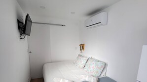 Une chambre avec un lit, un téléviseur fixé au mur, un climatiseur et un plancher en bois.