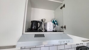 Une cuisine avec un plan de travail blanc, une bouilloire, une machine à café et un fer à repasser.