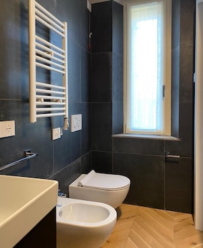 Et moderne badeværelse med toilet, bidet og et håndklædestativ.