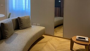 Un salon moderne avec un canapé aux lignes courbes, une petite table d’appoint en bois et un grand miroir qui reflète la pièce.