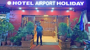 The exterior of Hotel Airport Holiday with a red facade, potted plants, and a man standing in front. - Hotel Airport Holiday (Kathmandu)