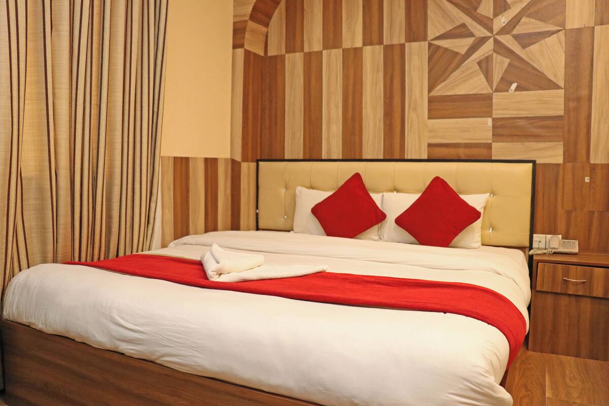 A hotel room with a large bed, red pillows, a wooden headboard, and a patterned wall.