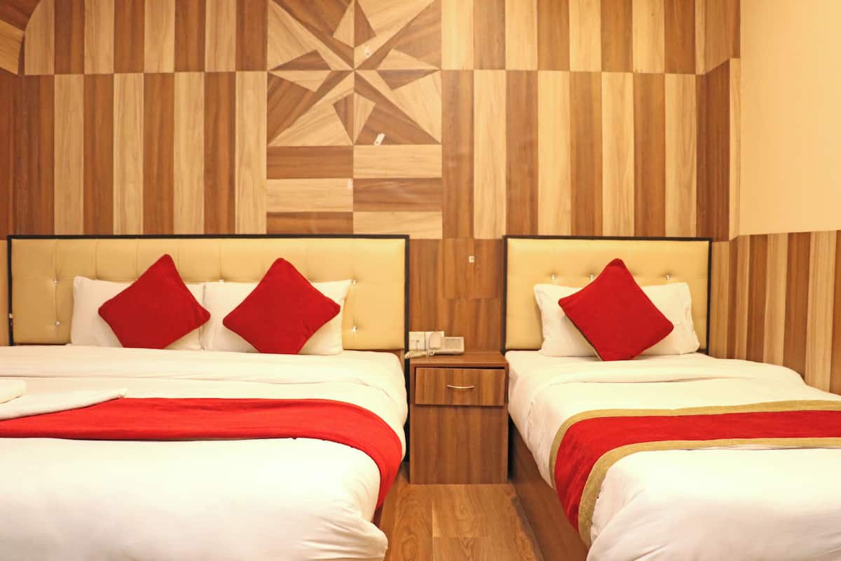 A hotel room with two beds, each with a red pillow and a wooden headboard. There is a wooden nightstand between the beds with a phone and a small drawer.