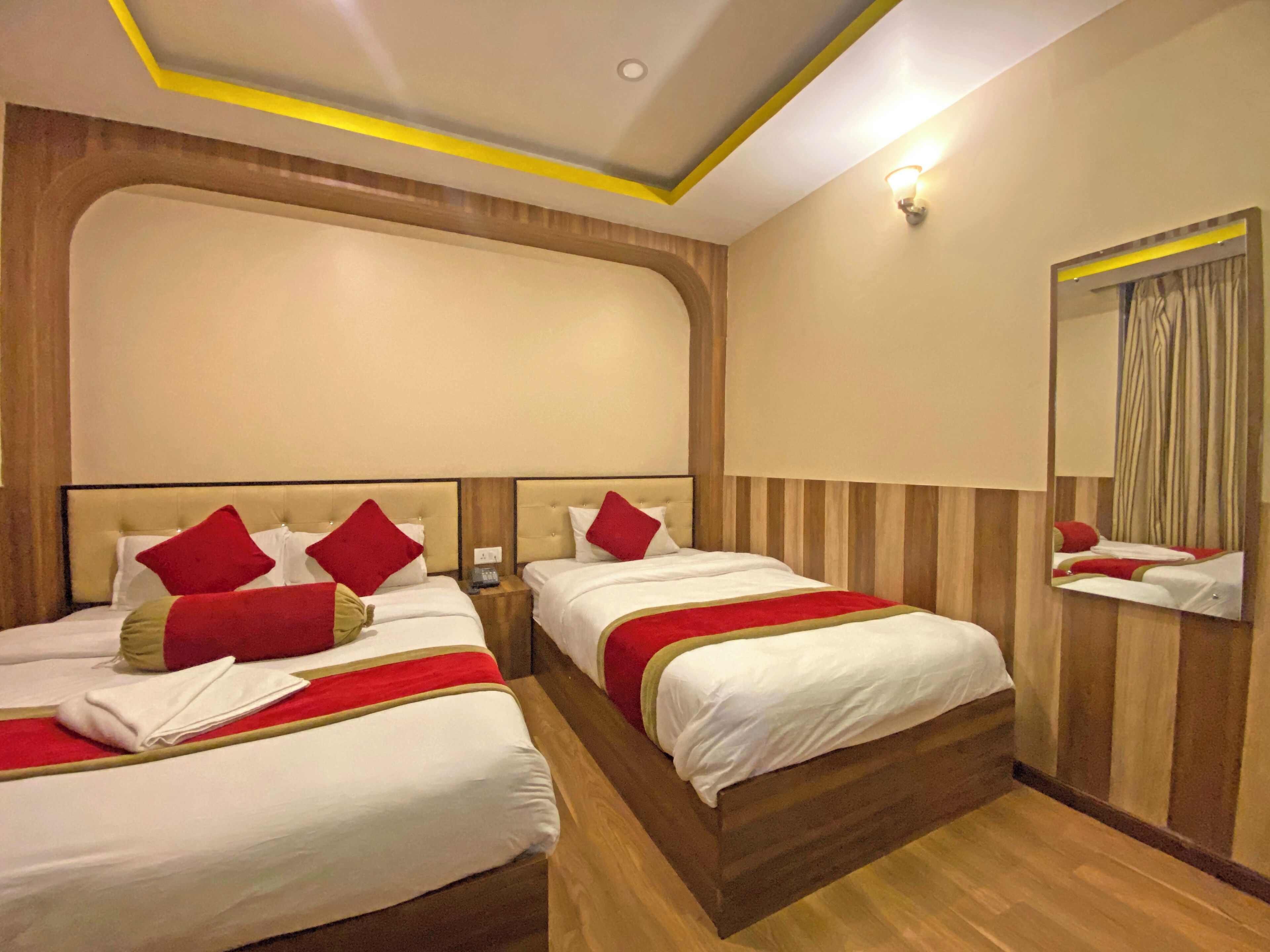 A hotel room with two beds, wooden headboards, a large mirror, and a wooden floor.