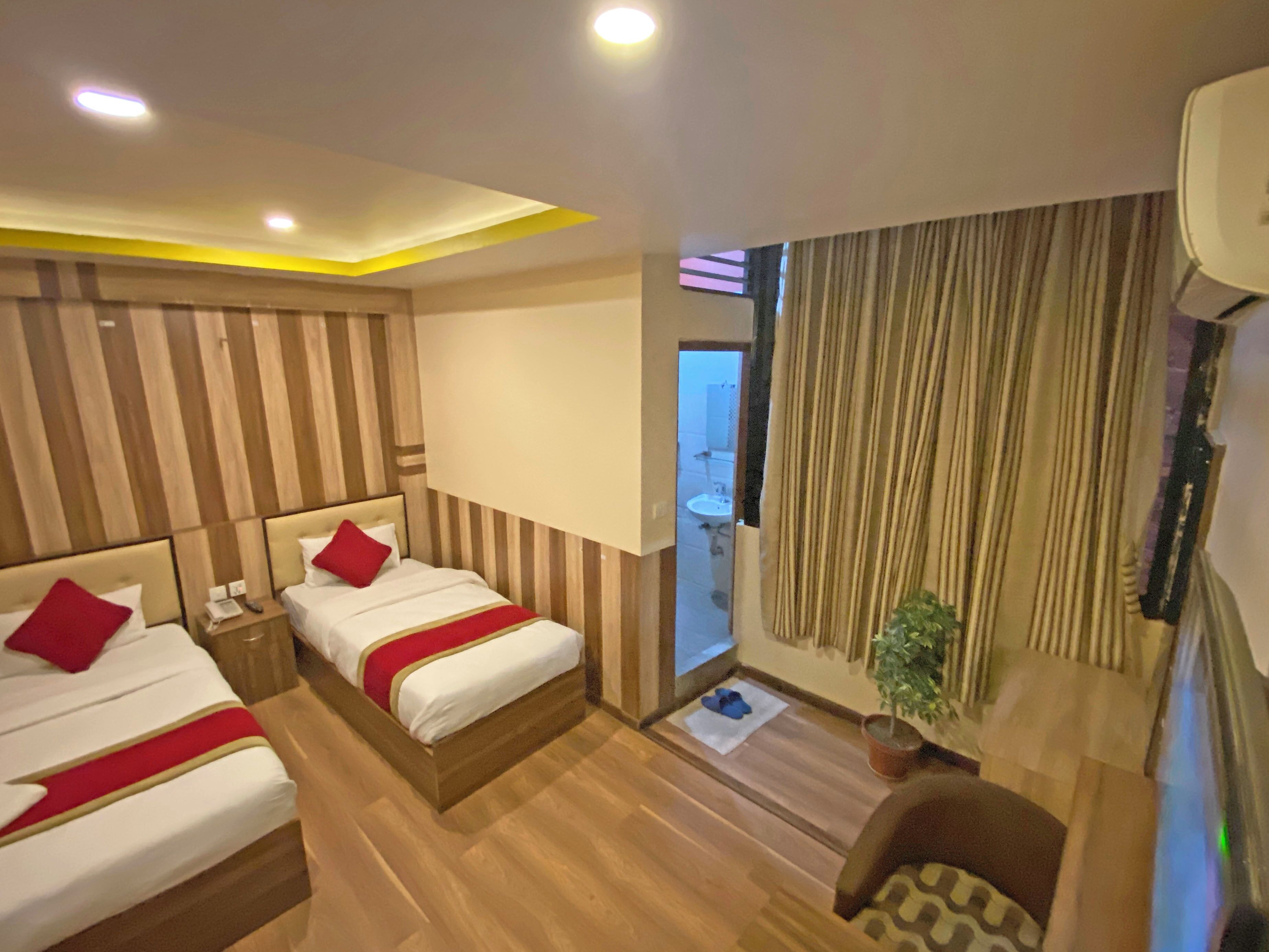 A hotel room with two beds, wooden flooring, a small seating area, and a view of the bathroom.