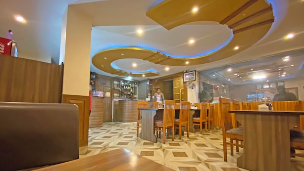 A restaurant with wooden booths and tables, a bar area, and a patterned floor. - Hotel Airport Holiday (Kathmandu)