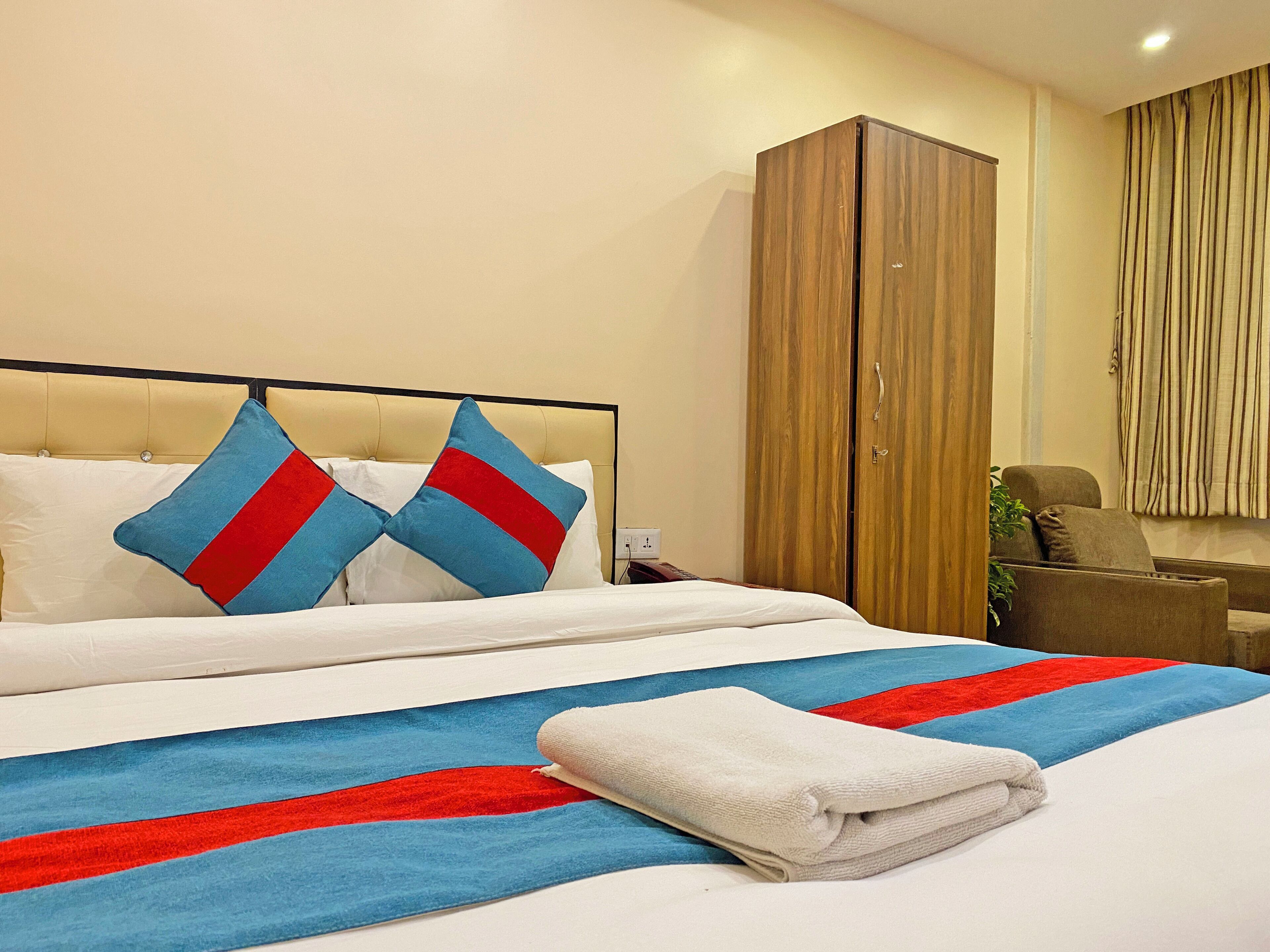 A hotel room with a bed, two pillows, a blanket, a wardrobe, and a chair.