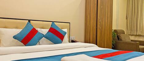 A hotel room with a bed, two pillows, a blanket, a wardrobe, and a chair.