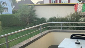 Een balkon met een tafel en stoelen, een metalen hekwerk en uitzicht op een gebouw met balkon.