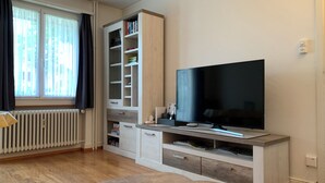 Een moderne woonkamer met een grote flatscreen-tv, een ingebouwde boekenkast en een ronde salontafel.
