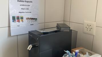 Una macchina per caffè con una vaschetta raccogligocce, un poster che pubblicizza capsule Delizio e una scatola di Espresso Delizio su un piano di lavoro in granito.