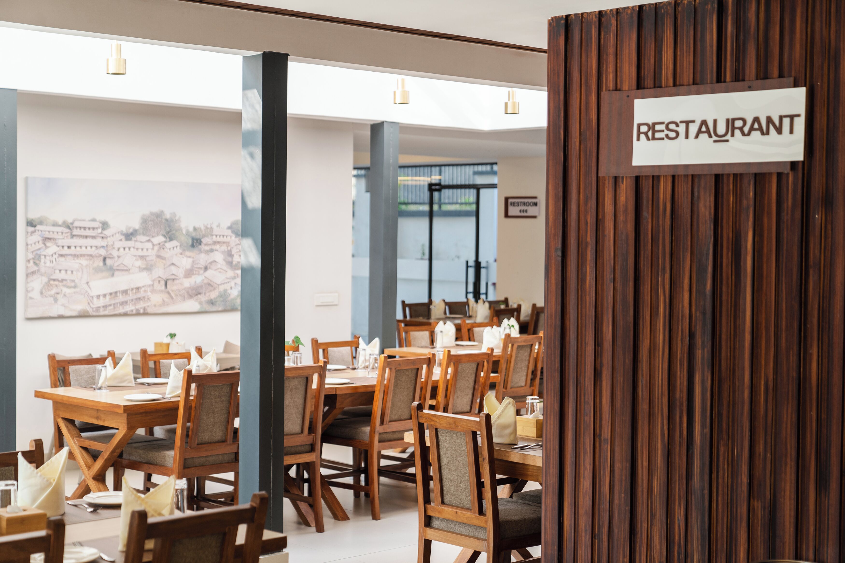A restaurant interior with wooden tables and chairs, a sign indicating the restaurant, and a view of buildings through the windows.